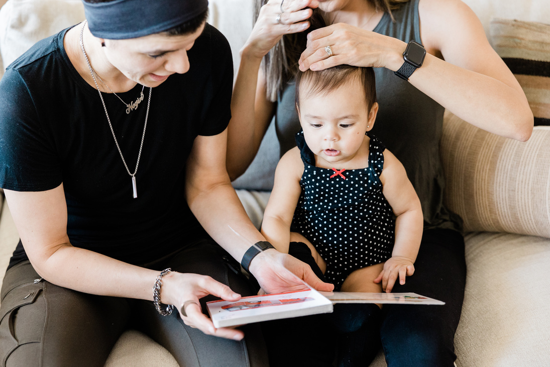 LGBT Couple with Baby Reading a Book on Sofa